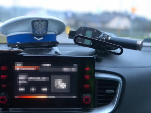 Na podszybiu radiowozu leży czapka policjanta ruchu drogowego oraz urządzenie do pomiaru prędkości.