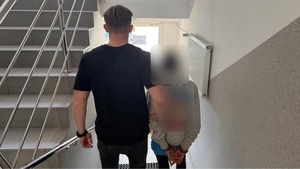 Policjanci podczas doprowadzenia zatrzymanego, który ma założone kajdanki na ręce trzymane z tyłu.